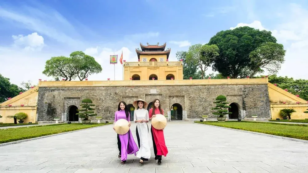 Cổng Đoan Môn Hoàng thành Thăng Long với ba cô gái mặc áo dài và nón lá đi trên sân gạch